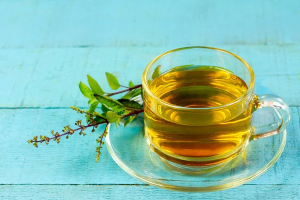 Tulsi ya da şeffaf cam fincanda mavi ahşap kaplamalı taze tütsü yaprağı olan kutsal fesleğen çayı. Hindistan 'da Ayurvedic tıp.