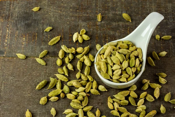 Yeşil kakule beyaz seramik kâse üzerinde ahşap arka planda. Yeşil kakule yemek pişirmek için kullanılan güzel kokulu bir bitkidir.. 