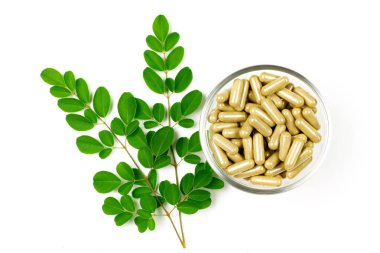 Moringa oleifera kapsülü cam kase üzerinde beyaz arka planda yalıtılmış bir yaprak ile.