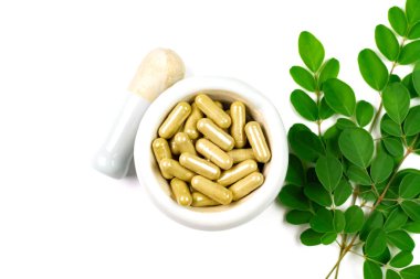 Moringa oleifera kapsülü beyaz zemin üzerinde izole bir moringa yaprağı ile havan ve tokmak.