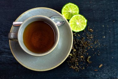 Bergamot çayı ya da seramik fincanda Earl Grey çayı ve siyah ahşap masada dilimlenmiş taze bergamot meyvesi..