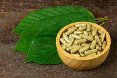Mitragyna Speciosa Korth veya kratom kapsülleri ahşap kapta yeşil yaprak ve kırsal ahşap masa üzerinde.