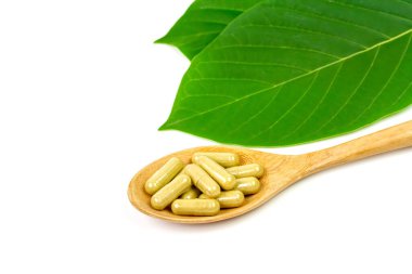Mitragyna Speciosa Korth veya kratom kapsülleri tahta kaşık üzerinde beyaz arkaplanda yeşil yaprak izole edilmiş.. 