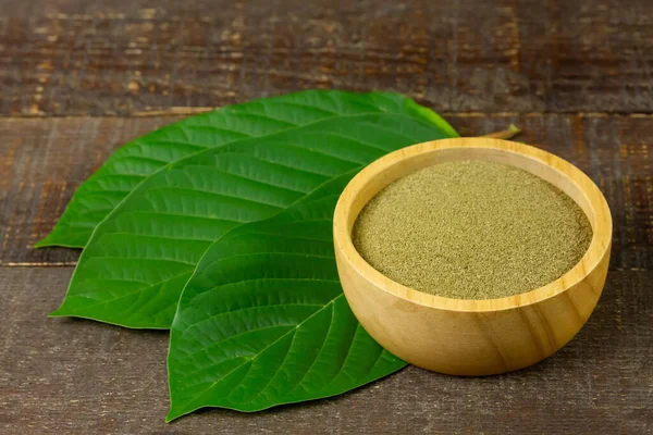 Mitragyna Speciosa Korth ya da tahta kase üzerinde kratom tozu kırsal ahşap arka planda yeşil yaprak. 