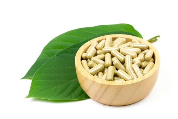 Mitragyna Speciosa Korth veya kratom kapsülleri beyaz arka planda yeşil yapraklı ahşap kase üzerinde. 
