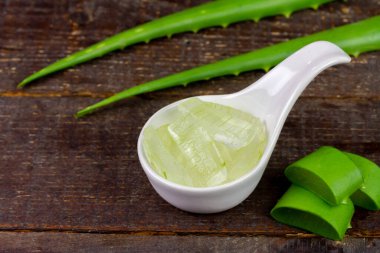 Aloe Vera jeli beyaz kasede, ahşap arka planda taze aloe vera ile..