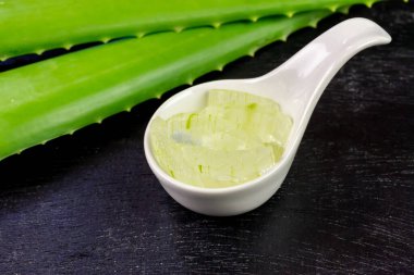 Aloe Vera jeli beyaz kasede, siyah ahşap arka planda taze aloe vera ile..