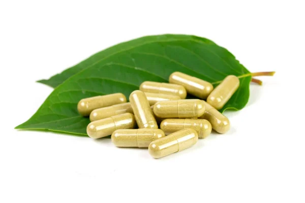Beyaz arkaplanda yeşil yapraklı Mitragyna Speciosa Korth veya kratom kapsülleri. 