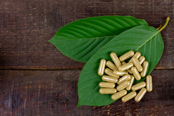 Mitragyna Speciosa Korth veya kratom kapsülleri kırsal ahşap masa üzerinde yeşil yaprak, üst görünüm.
