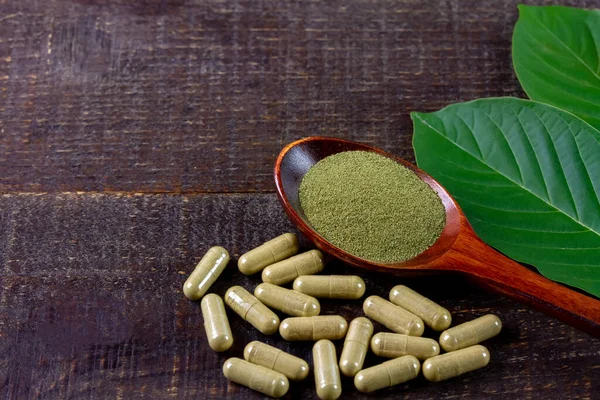 Mitragyna Speciosa Korth veya kratom kapsülleri ahşap kaşık üzerinde yeşil yaprak ve kırsal ahşap masa üzerinde kapsüller, kopyalama alanı, üst görünüm.