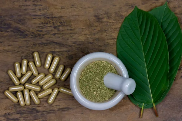 Mitragyna Speciosa Korth veya kratom kapsülleri kırsal ahşap masa üzerinde beyaz havan topuzu ve yeşil yaprak, üst görünüm, kopyalama alanı.