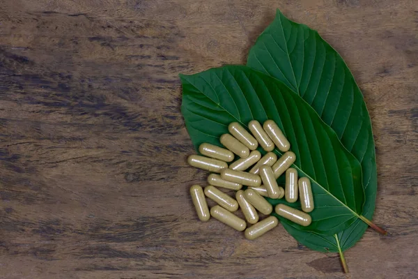 Mitragyna Speciosa Korth veya kratom kapsülleri kırsal ahşap masa üzerinde yeşil yaprak, üst görünüm.