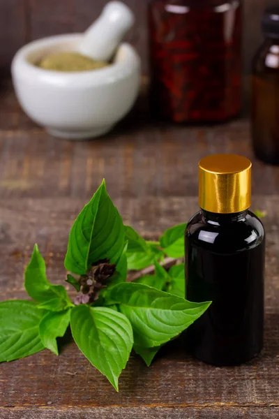 Bottle of basil essential oil with fresh basil leaf on rustic wooden background. Basil is both food and herbs for health care.