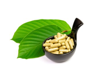 Mitragyna Speciosa Korth veya kratom kapsülleri beyaz arka planda yeşil yapraklı siyah kase üzerinde.