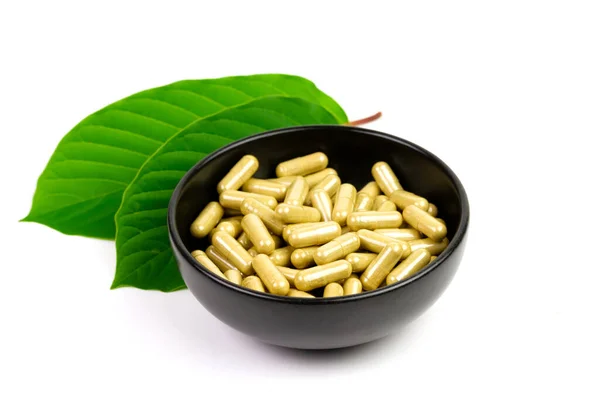 Mitragyna Speciosa Korth veya kratom kapsülleri beyaz arka planda yeşil yapraklı siyah kase üzerinde.