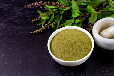Holy basil powder on white bowl with branch on black wooden background. Holy basil leaf are useful herbs and food ingredient has a spicy flavor. 