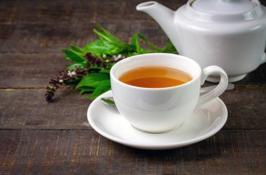 Basil tea in white cup ceramic with green leaf and white teapot on rustic wooden table. Basil is food and herb for healthy.