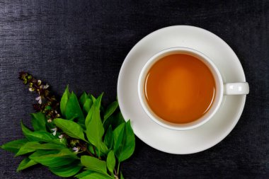 Basil tea in white cup ceramic with green leaf on black wooden table, top view, copy space. Basil is food and herb for healthy.