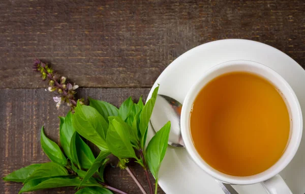 Basil tea in white cup ceramic with green leaf on rustic wooden table, top view. Basil is food and herb for healthy.