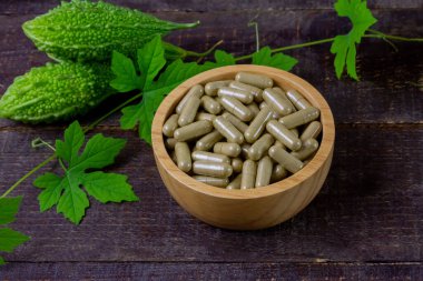 Bitter gourd or bitter melon capsules on wooden bowl and fresh bitter gourd with green leaf on rustic wooden table. Scientific name is Momordica charantia. 