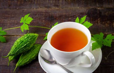 Bitter gourd or bitter melon tea in ceramic cup with fresh bitter gourd and green leaf on rustic wooden table. Scientific name is Momordica charantia. As a whole food and herbs for treating diseases.