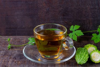 Bitter gourd or bitter melon tea in transparent cup and fresh bitter gourd with green leaf on rustic wooden table. Scientific name is Momordica charantia. 
