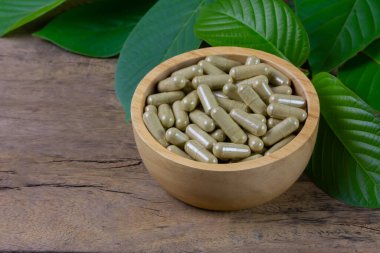 Mitragyna Speciosa Korth or kratom capsules in wooden bowl with green leaf on rustic wooden table.