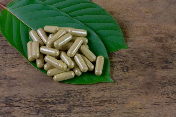 Mitragyna Speciosa Korth veya kratom kapsülleri kırsal ahşap masa üzerinde yeşil yaprak, üst görünüm.