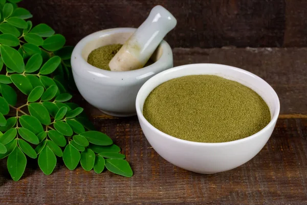 Moringa oleifera powder in white cup with mortar and pestle and green leaf on rustic wooden table. Moringa is a food and herb for health care.