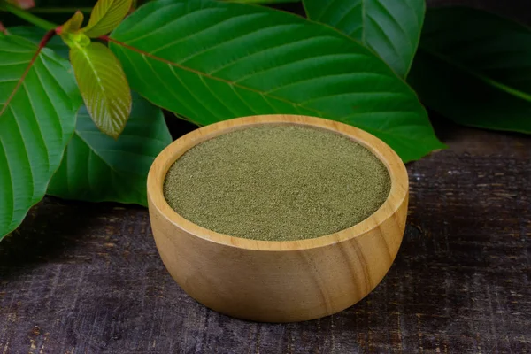 Mitragyna Speciosa Korth or kratom powder on wooden bowl wtih green leaf on rustic wooden table.