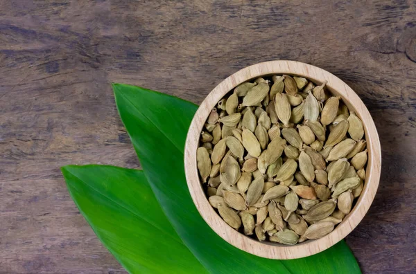 Green Cardamom on wooden bowl with green leaf on rustic wooden table, top view. Cardamom is a fragrant herb used as an ingredient for cooking.