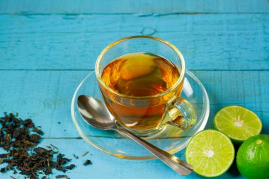 Hot tea in glass cup with fresh lime on blue wooden background.