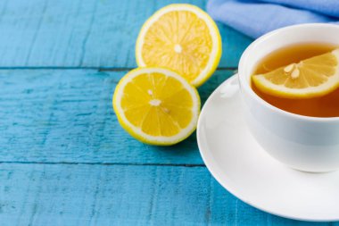 Cup of hot tea and lemon on blue wooden table.