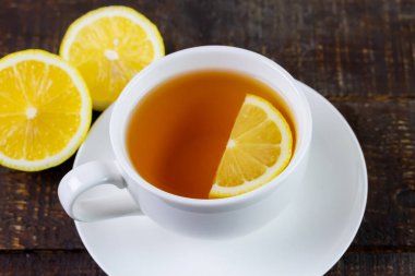Cup of hot tea in white ceramic cup and fresh lemon on rustic wooden table.