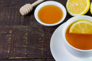 Cup of hot tea in white ceramic cup and fresh lemon on rustic wooden table.