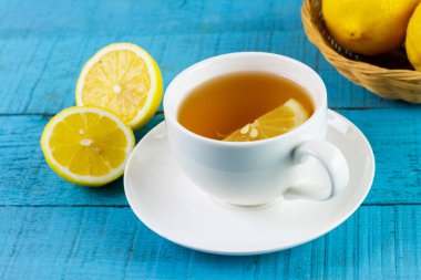 Cup of hot tea in white ceramic cup and fresh lemon on blue wooden table.