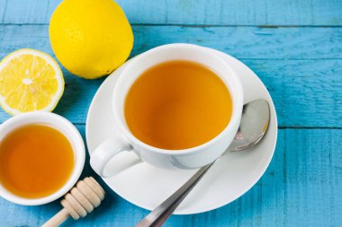 Cup of hot tea in white ceramic cup and fresh lemon on blue wooden table.