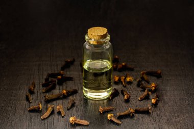 Şişedeki karanfil yağı ve siyah ahşap arka plandaki kuru karanfiller..
