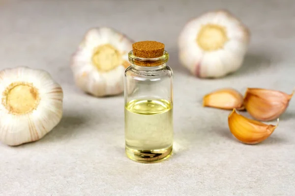 Garlic oil in transparent bottle with Garlic Cloves on rough surface background.