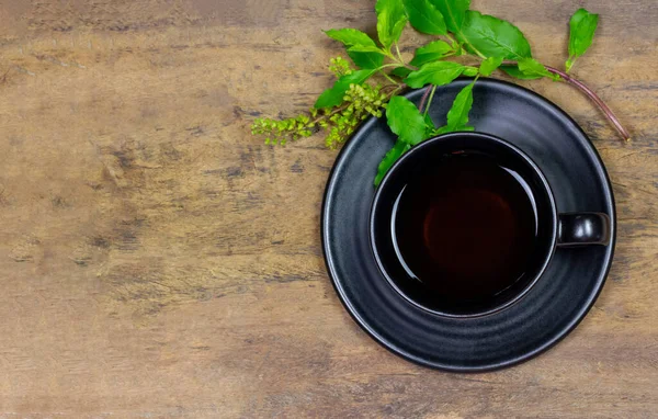 图尔西或神圣罗勒茶在黑色陶瓷杯与郁金香叶和枝条在乡村木桌上 顶部视图 印度的Ayurvedic医学 为健康饮酒 — 图库照片