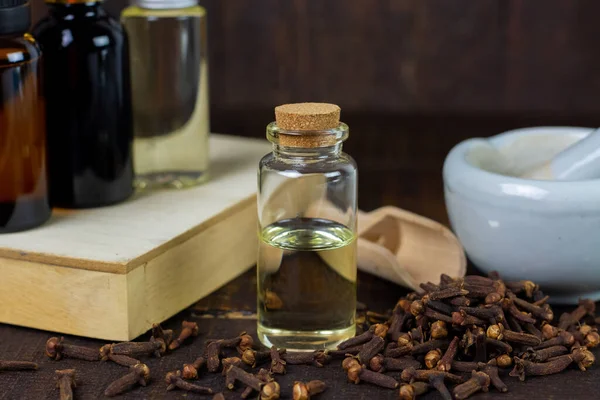 Essential oil of cloves in bottle and dry cloves on rustic wooden background.