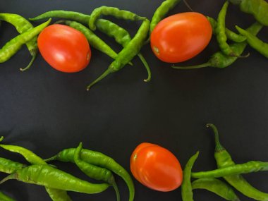 Koyu bir arka planda doğal domates ve biber. Gıda arkaplanlı üst görünüm, siyah taş tablo, kopyalama alanı.