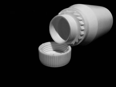 The empty plastic white bottle is on a dark background.