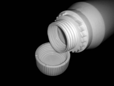 The empty plastic white bottle is on a dark background.