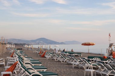 Akşam Alanya plajında, deniz ve dağların zeminine karşı boş güneş şezlongları, Türkiye, Kasım 2021.