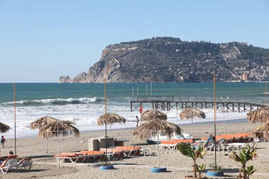 Plaj şemsiyeleri fırtınalı bir denizin ve tarihi bir dağ olan Alanya 'nın arka planına karşı, Aralık 2021.