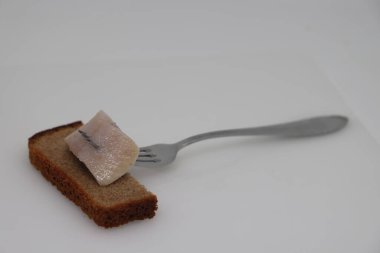 Pieces of salted herring on fork on white backgrod.