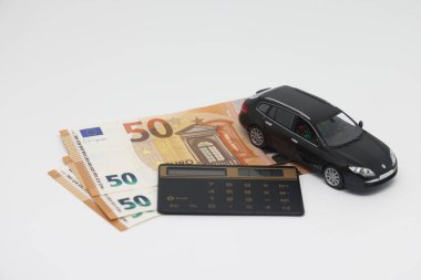 Oyuncak bir araba ve banknotlar mutfak elektronik terazisinde bir hesap makinesinin yanında durur..