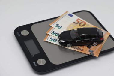 Oyuncak bir araba ve banknotlar mutfak elektronik terazisinde bir hesap makinesinin yanında durur..