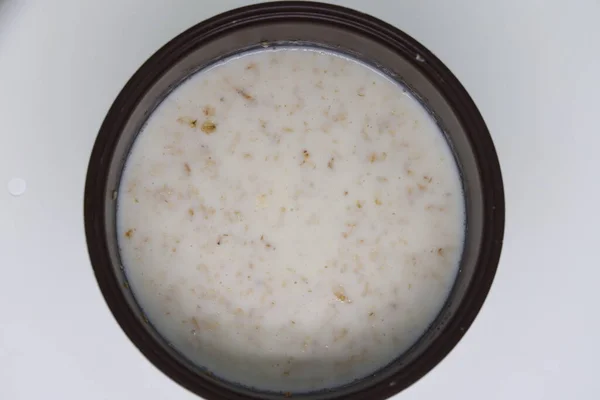 Oatmeal in a metal pot is cooked in a cooker. Close up photo.